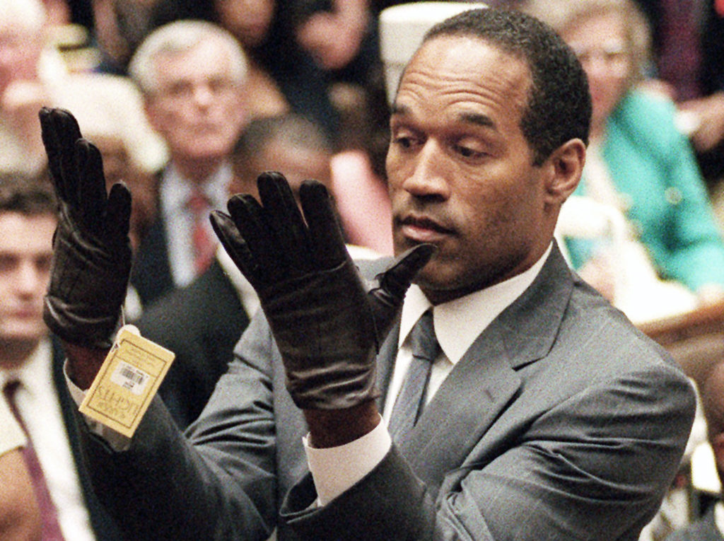 FILE - June 21, 1995 file photo, O.J. Simpson holds up his hands before the jury after putting on a new pair of gloves similar to the infamous bloody gloves during his double-murder trial in Los Angeles. Associated Press writer Linda Deutsch is seen in the background at right; writer Dominick Dunne is in the background at left rear. (AP Photo/Vince Bucci, Pool, File) ** Usable by LA and DC Only **